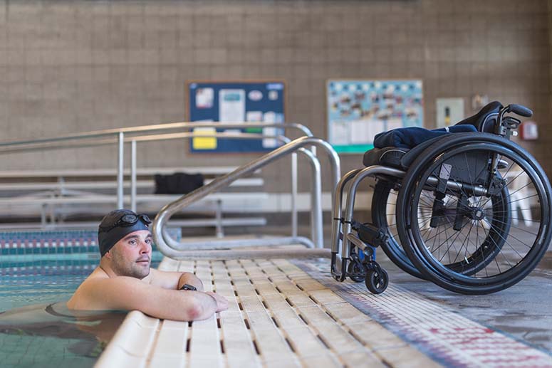 Man in swimming pool by wheelchair